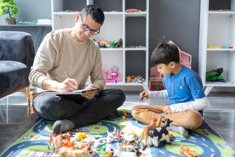 Child psychologist playing with young child on toy mat